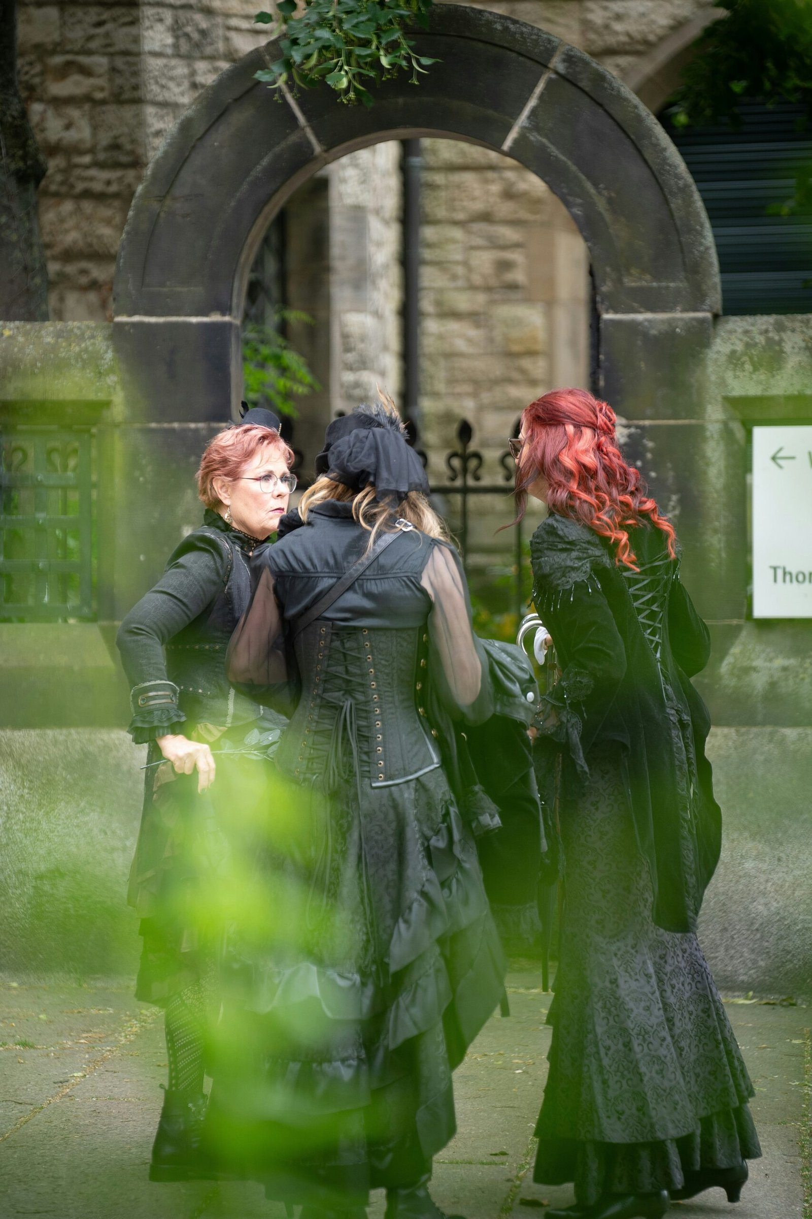 three women dressed in green and black standing in front of a building